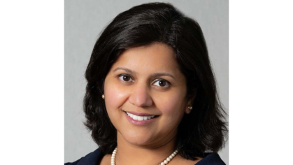 A person with short dark hair wearing pearl earrings and a pearl necklace.